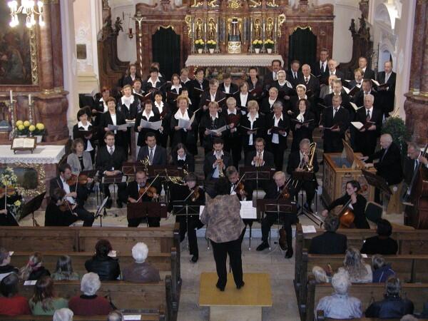 Chor und Orchester in voller Aufführung in einer Kirche, Zuschauer im Hintergrund.